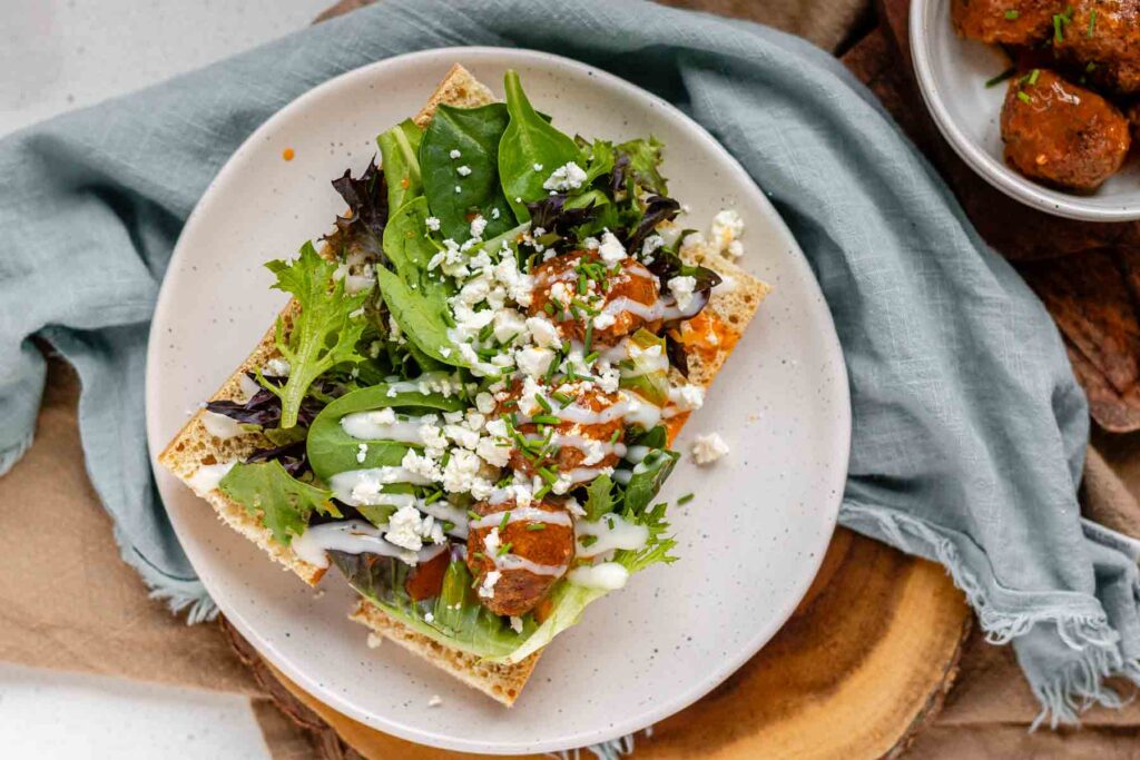 An open sandwich with meatballs, greens, and sauce.