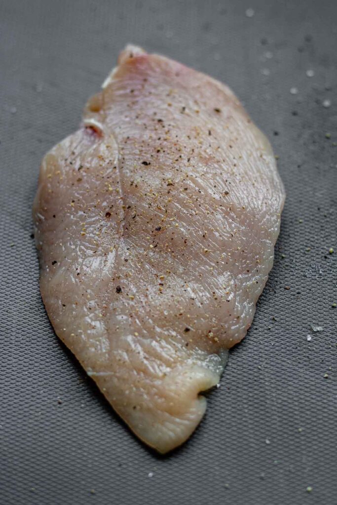 A chicken breast with salt and pepper.