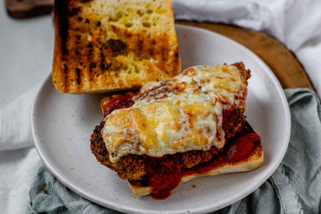 An open sandwich with breaded chicken, red sauce, and melted cheese.