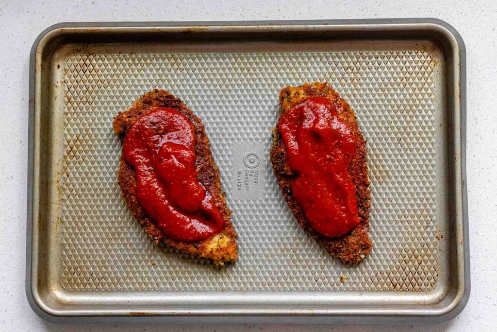 Fried chicken coated in breadcrumbs, topped with red sauce.