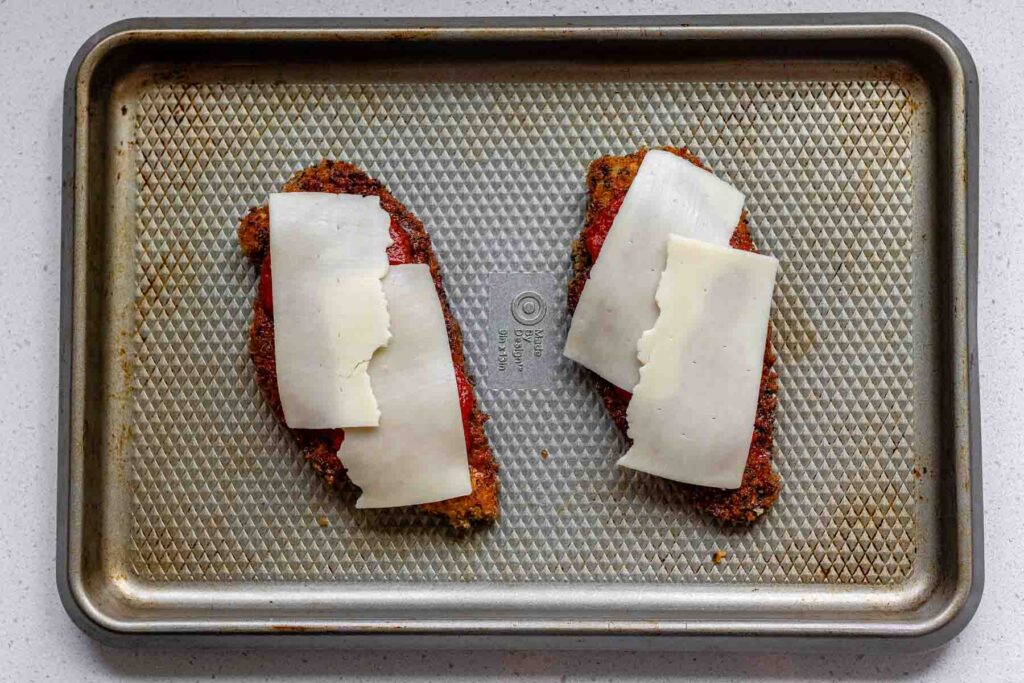 Fried chicken coated in breadcrumbs, topped with red sauce, and cheese.