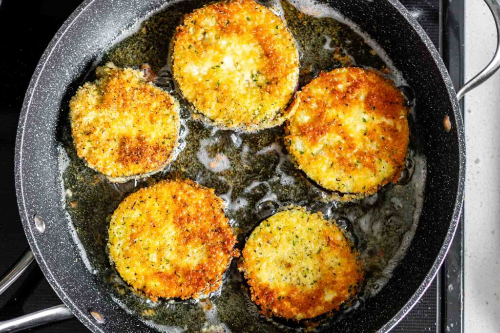 Breaded eggplant slices frying in oil in a skillet.