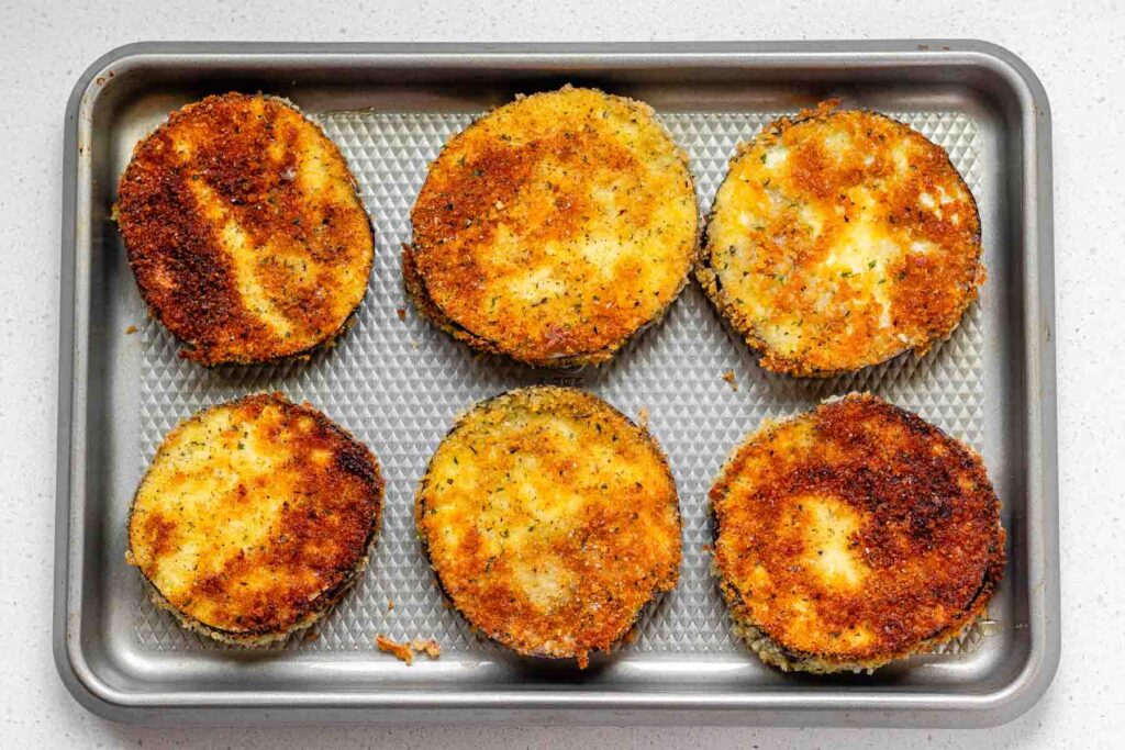 Breaded eggplant slices on a sheet pan.