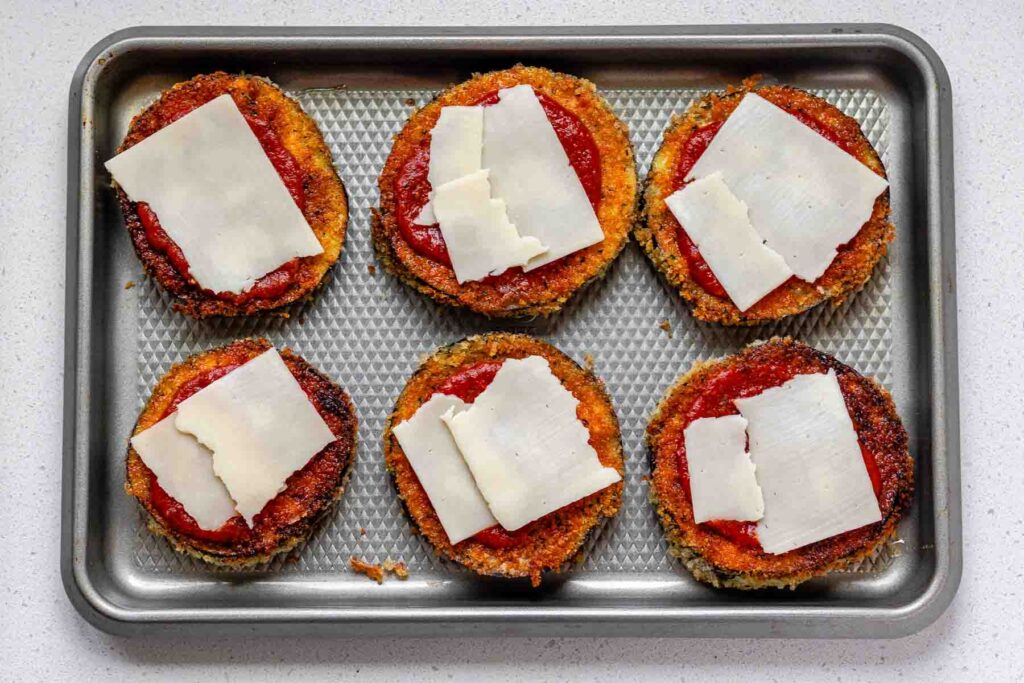 Breaded eggplant slices on a sheet pan with tomato sauce and cheese on top.