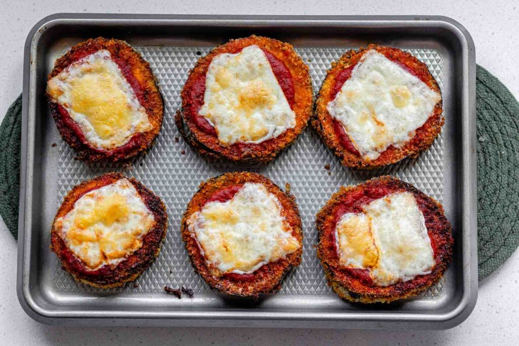 Breaded eggplant slices on a sheet pan with tomato sauce and browned cheese on top.