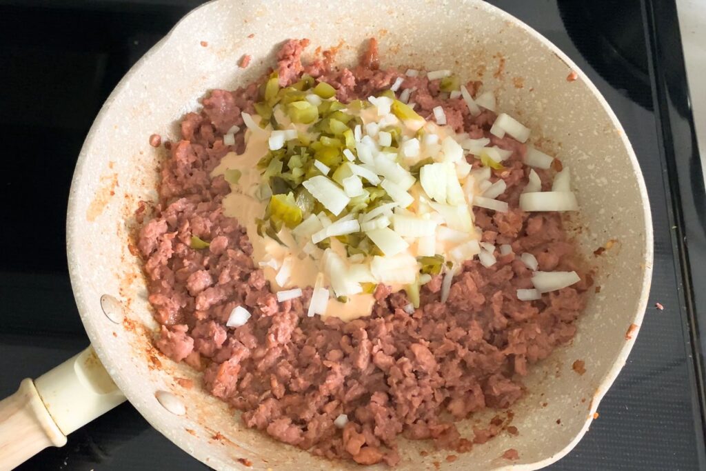 Beef, Big Mac sauce, onion, and pickle in a frying pan.