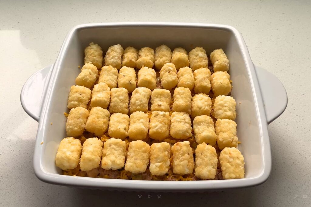 Beef and cheese in a white baking dish lined with tater tots.