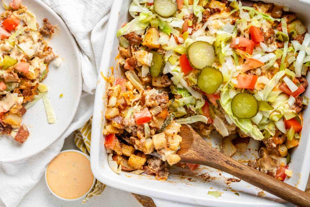 Big Mac casserole in a white casserole dish with a wooden spoon.