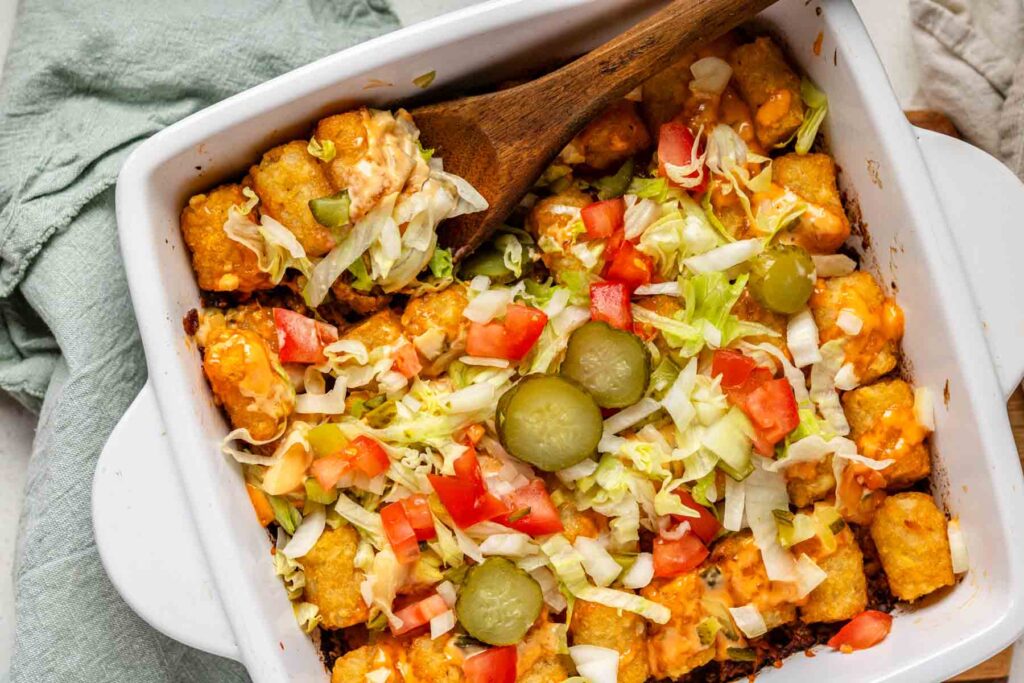 Big Mac tater tot casserole in a white baking dish with a spoon scooping a portion.