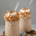 Two milkshakes topped with whipped cream and cereal.