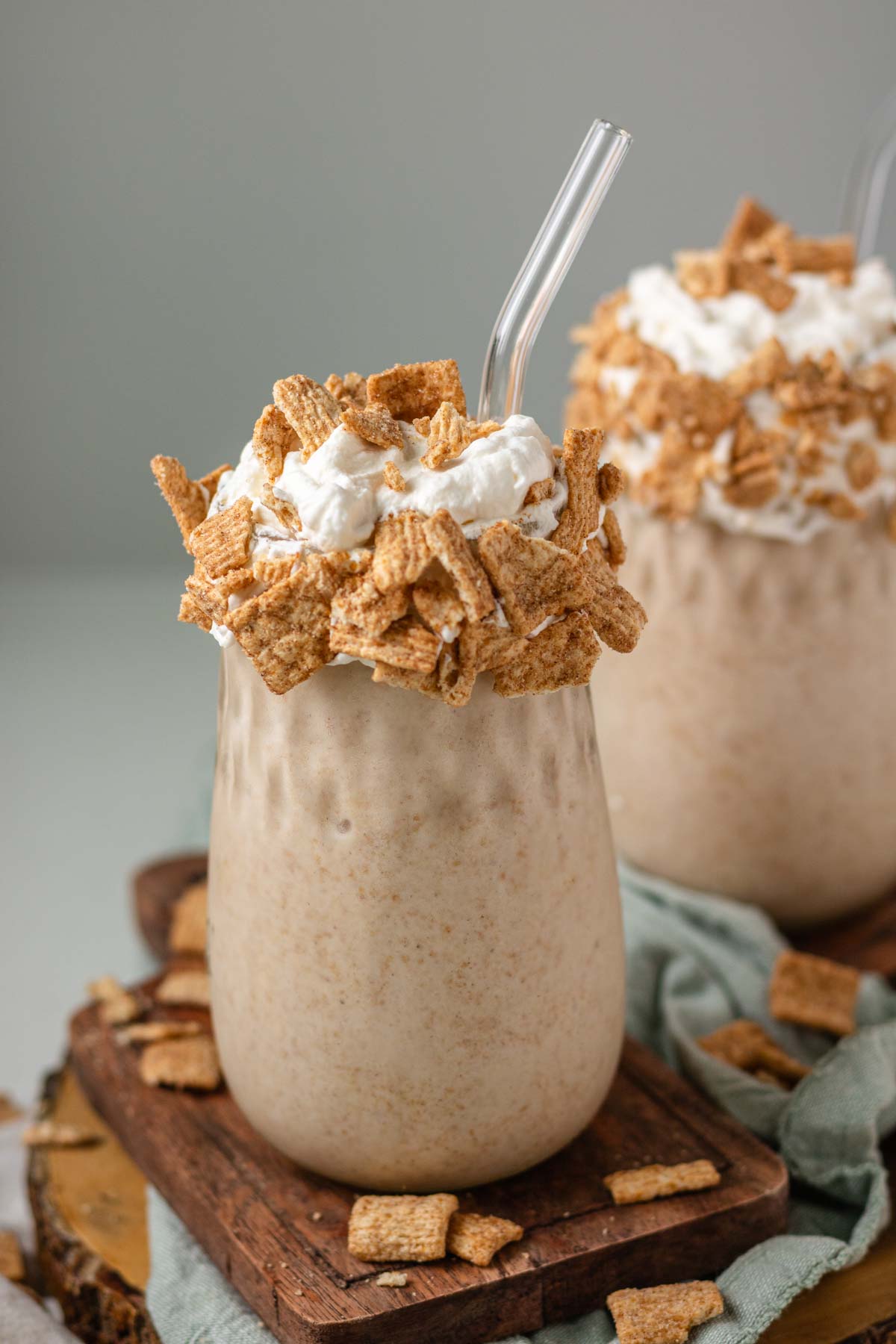 A milkshake in a glass jar topped with whipped cream, cereal and a glass straw.