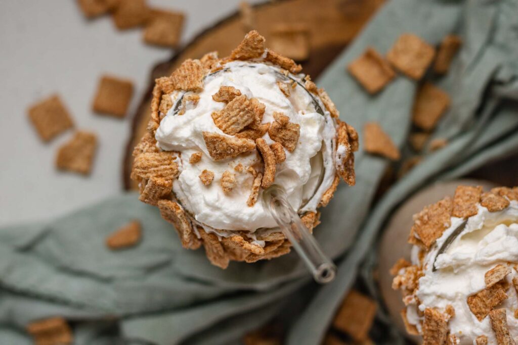 Top down view of a milkshake topped with whipped cream and cereal.