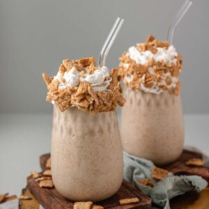 Two milkshakes in a glass jars topped with whipped cream and cereal.