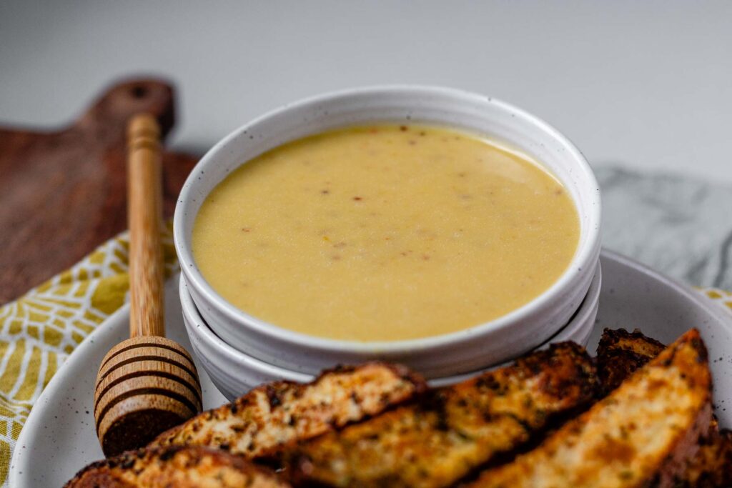 Yellow sauce in a bowl on a plate with potato wedges.