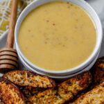 Yellow sauce in a bowl on a plate with potato wedges.