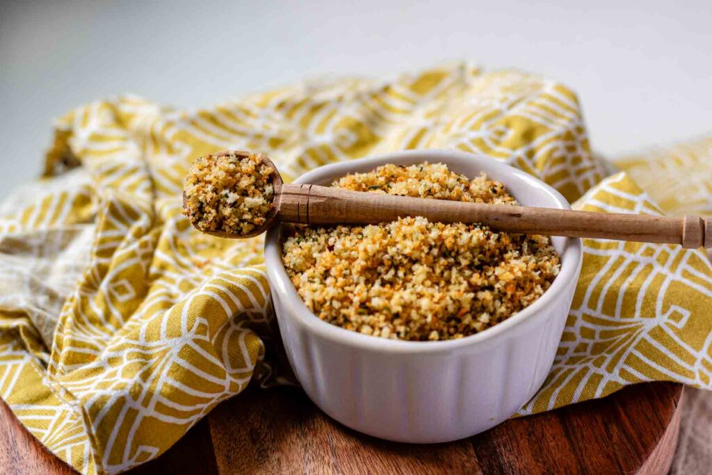 A bowl of toasted breadcrumbs with a spoon of breadcrumbs resting on top.