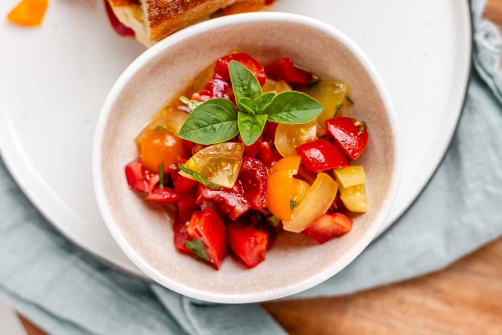 A bowl with diced tomatoes, topped with oregano leaves.