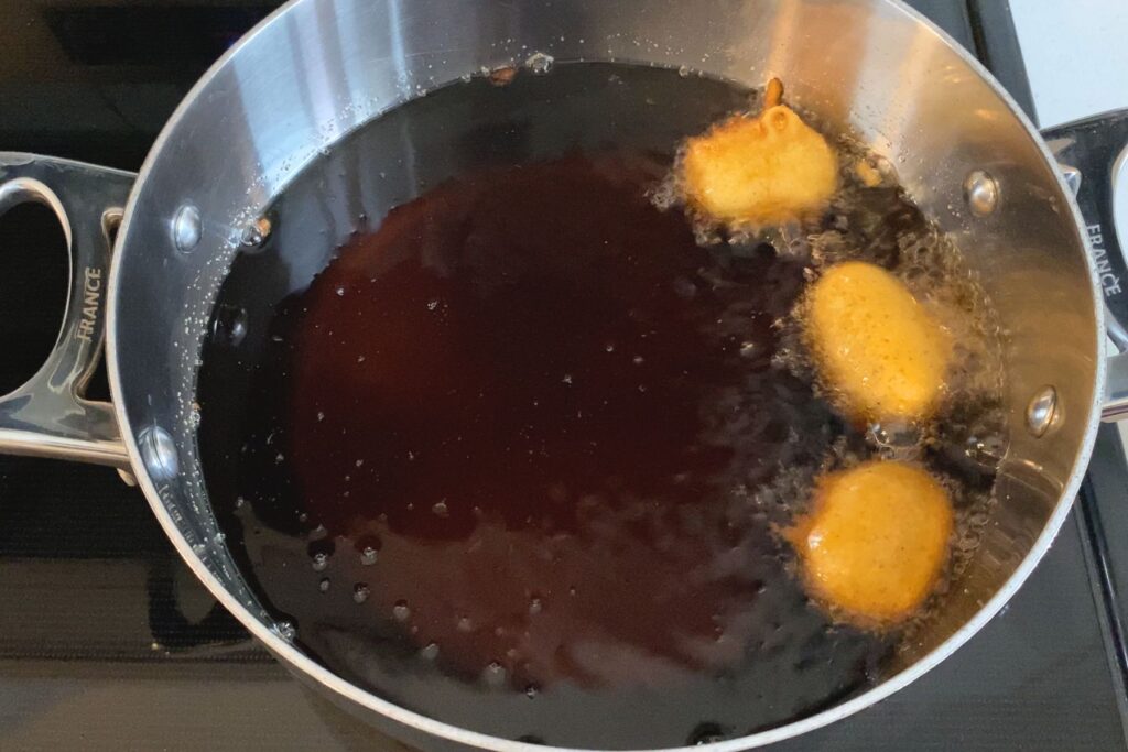 Three corn dog nuggets frying in a pot of oil.