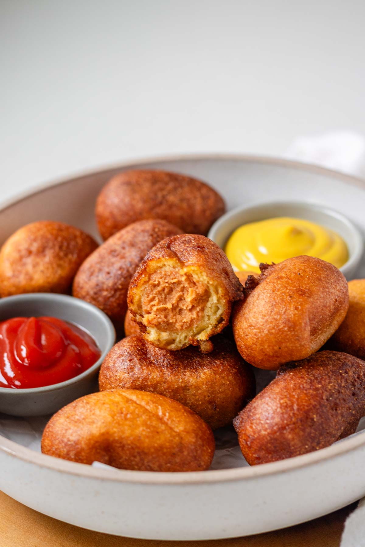 Corn dog nuggets in a bowl with one in half, showing the inside.