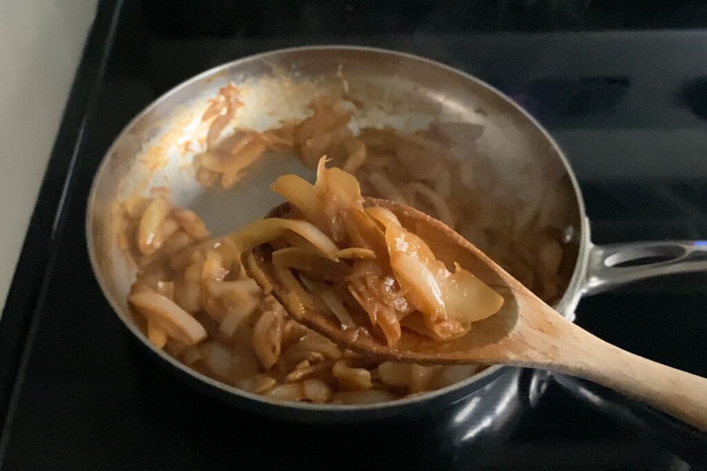 Caramelized onions on a wooden spoon above a stainless steel pan.