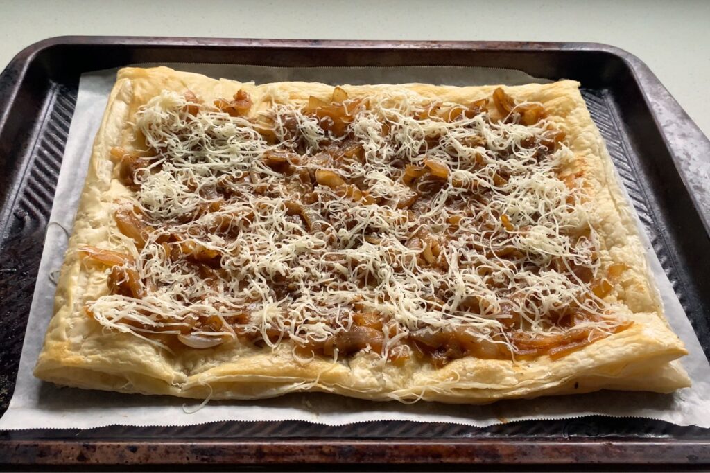 Baked puff pastry topped with caramelized onions and shredded cheese.