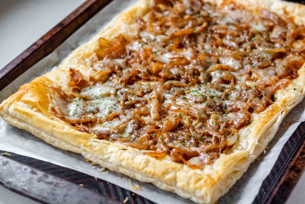 A close up of caramelized onions and melted cheese on top of puff pastry.