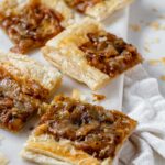Squares of puff pastry topped with caramelized onions and melted cheese on a marble slab.
