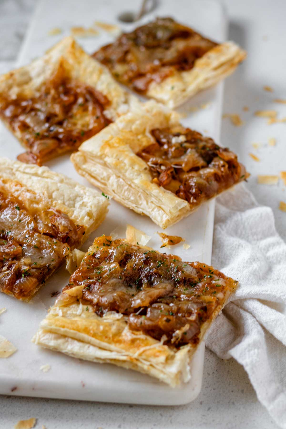 Squares of puff pastry topped with caramelized onions and melted cheese on a marble slab.