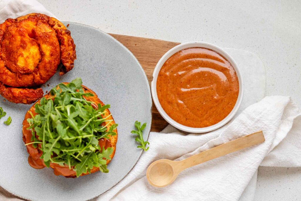 Bbq mayo in a bowl beside a burger on a plate.