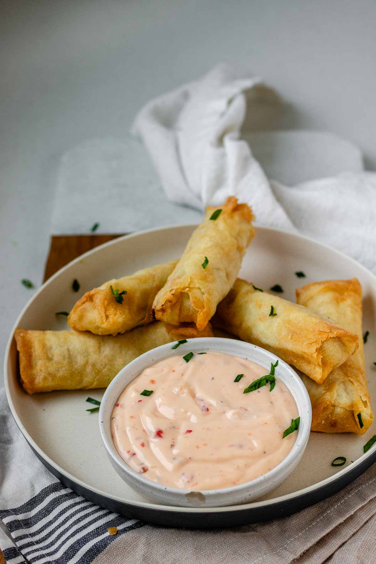 Sweet chili mayo in a bowl on a plate beside spring rolls.