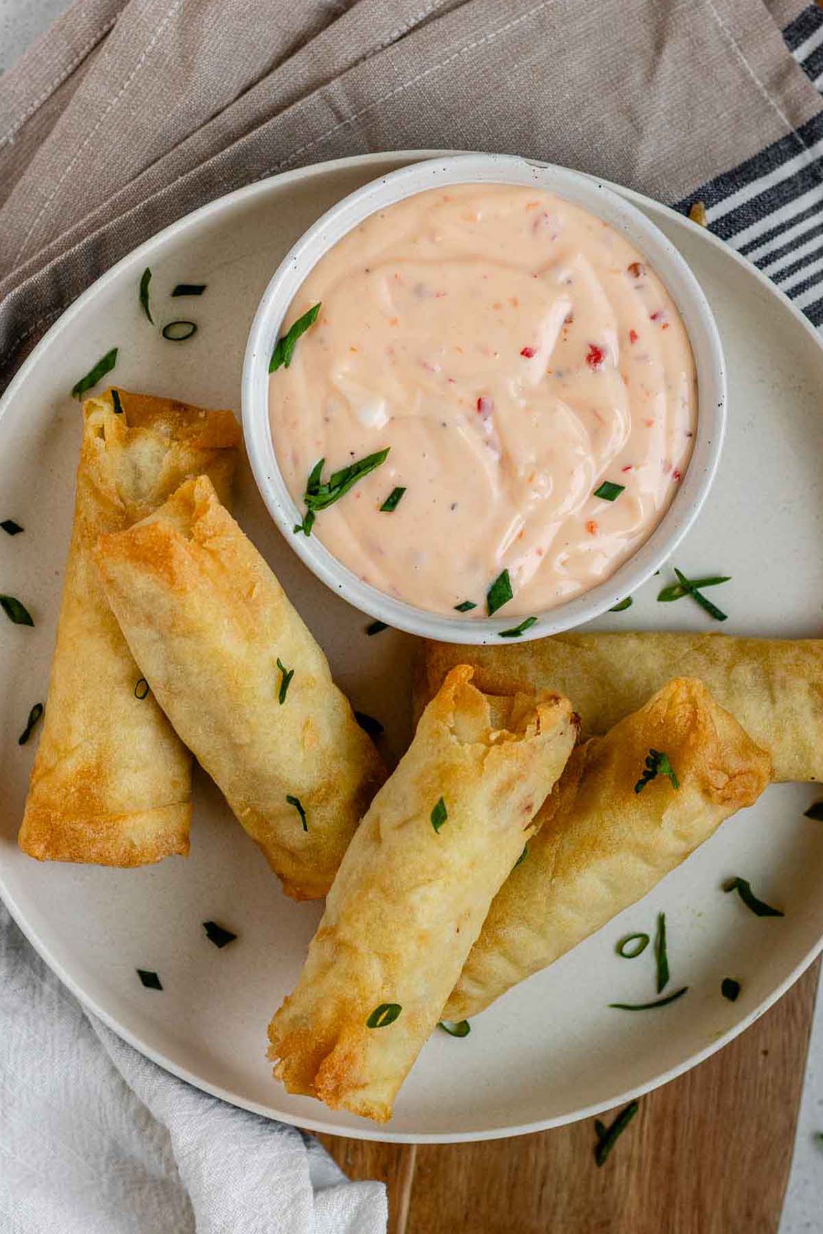 Sweet chili mayo in a bowl on a plate beside spring rolls.