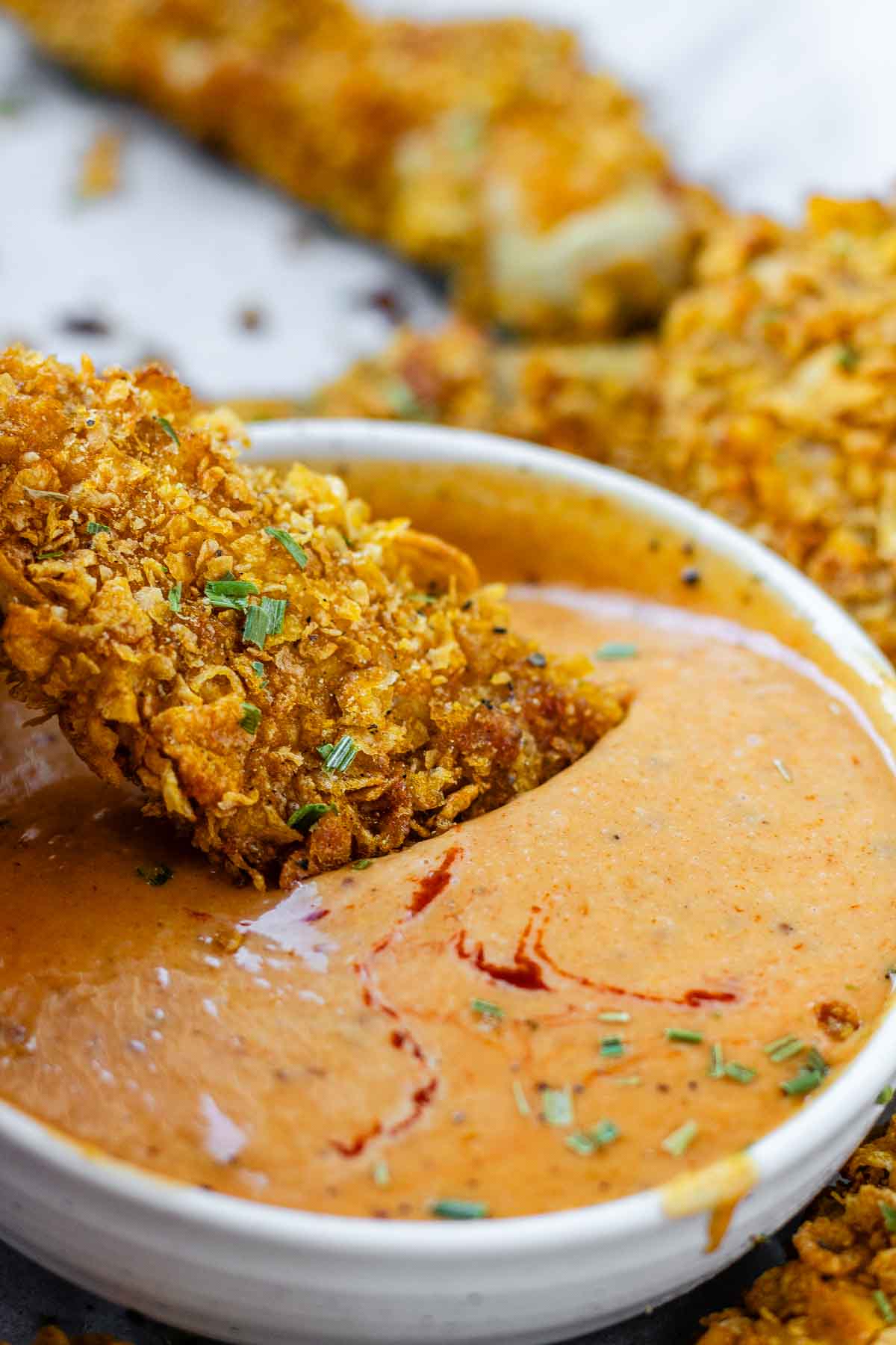 Orange sauce in a bowl with a chicken strip being dipped into it.