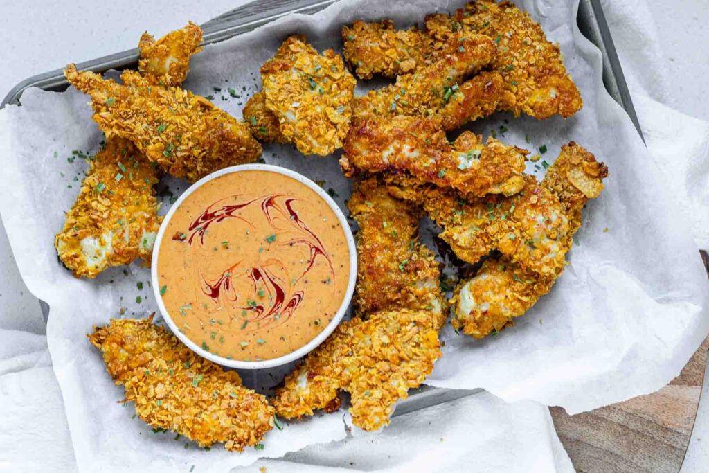 Orange sauce in a bowl surrounded by chicken strips.