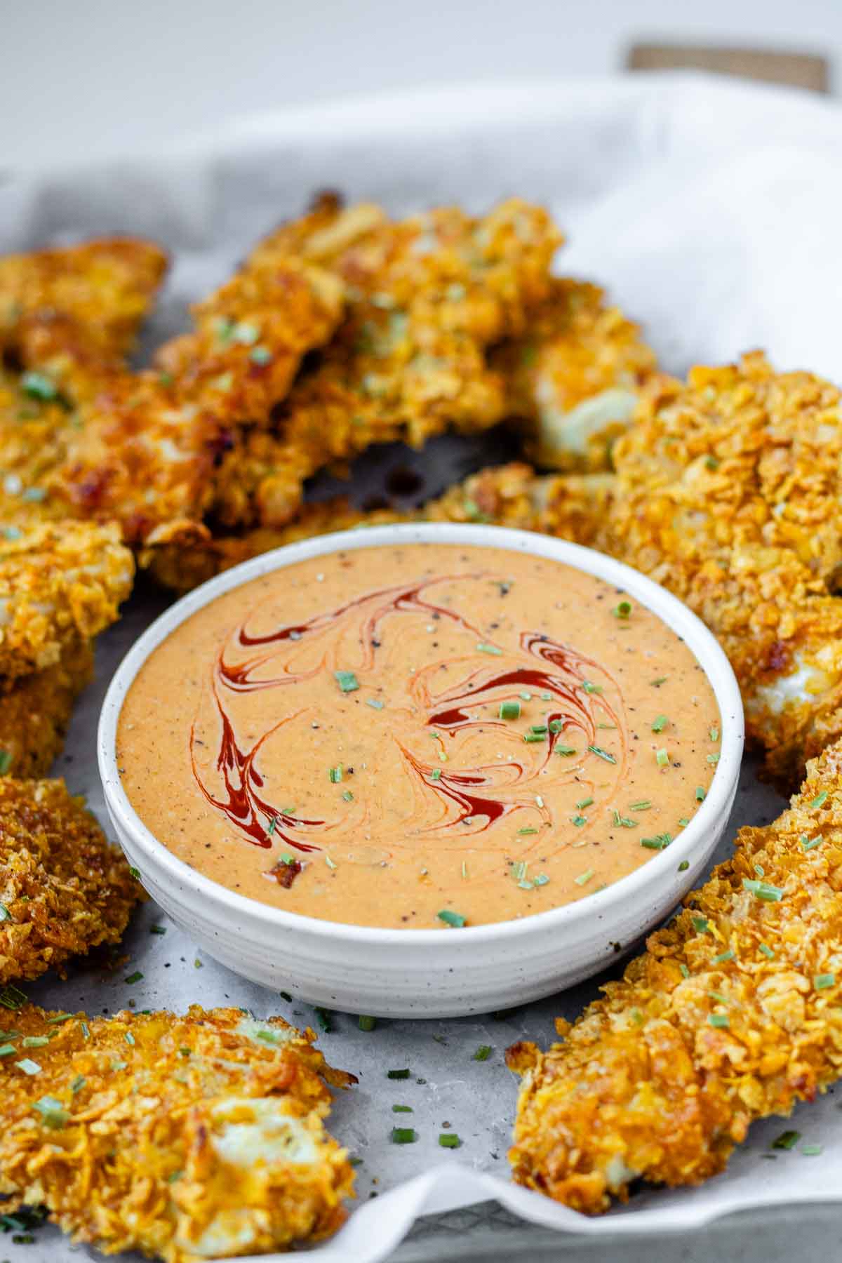Orange sauce in a bowl surrounded by chicken strips.