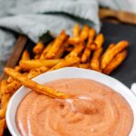 Orange sauce in a bowl surrounded by fries.