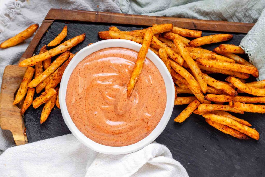 Orange sauce in a bowl surrounded by fries.