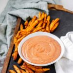Orange sauce in a bowl surrounded by fries.